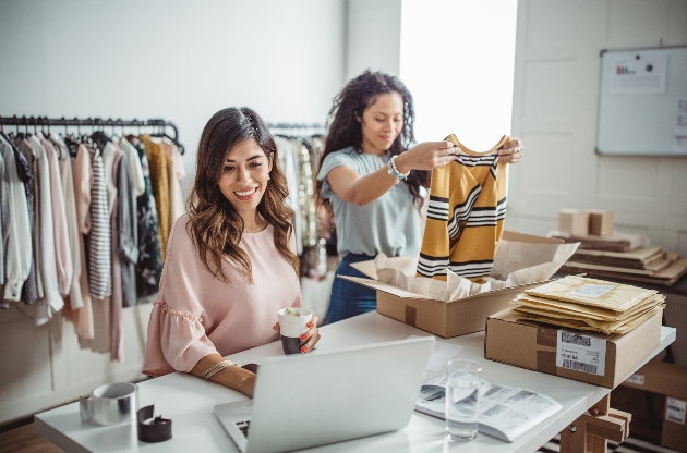 two women in a warehouse sorting stock and sitting at a laptop