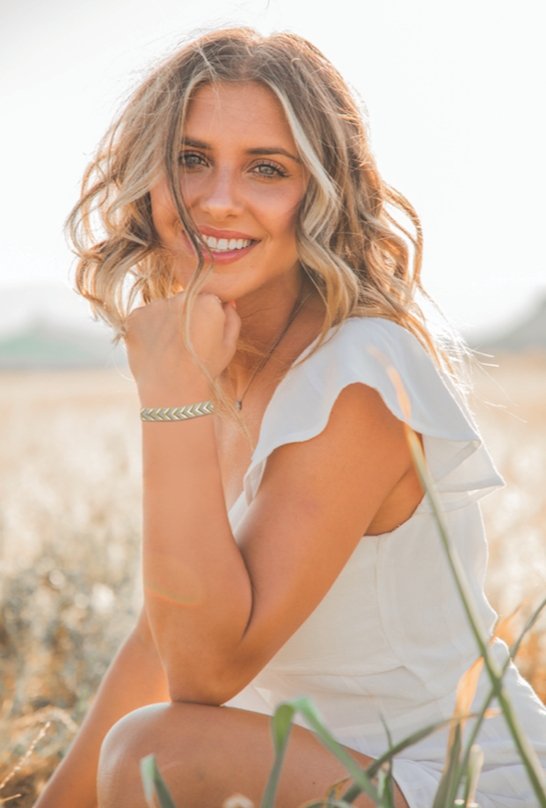 woman in a field on a sunny day bent down showing her bracelet