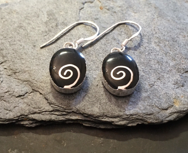 silver earring with black and silver detail laying on a rock