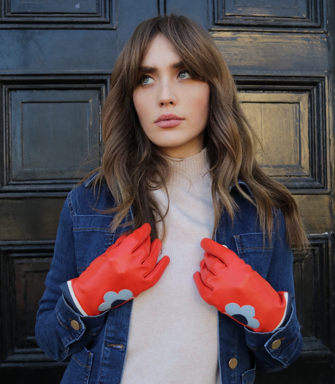 woman standing in a blue denim jacket wearing red leather gloves