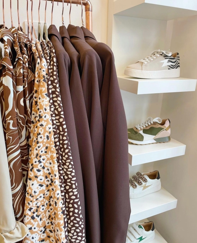 brown and cream coloured clothes on a rail with shelves of trainers