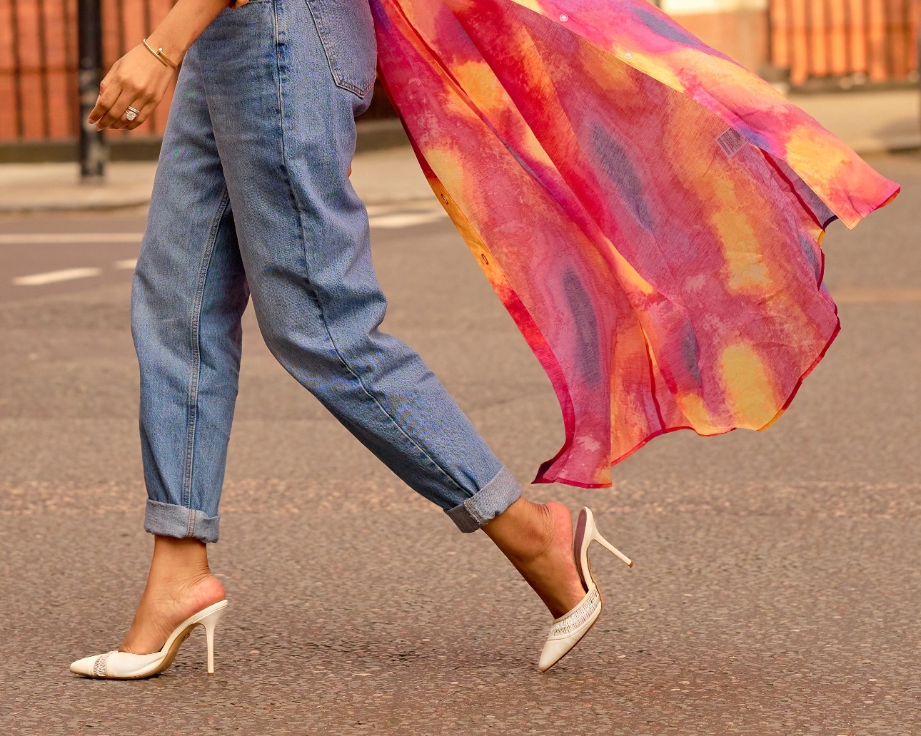 model wearing jeans and pair of heeled shoes walking on a pavement