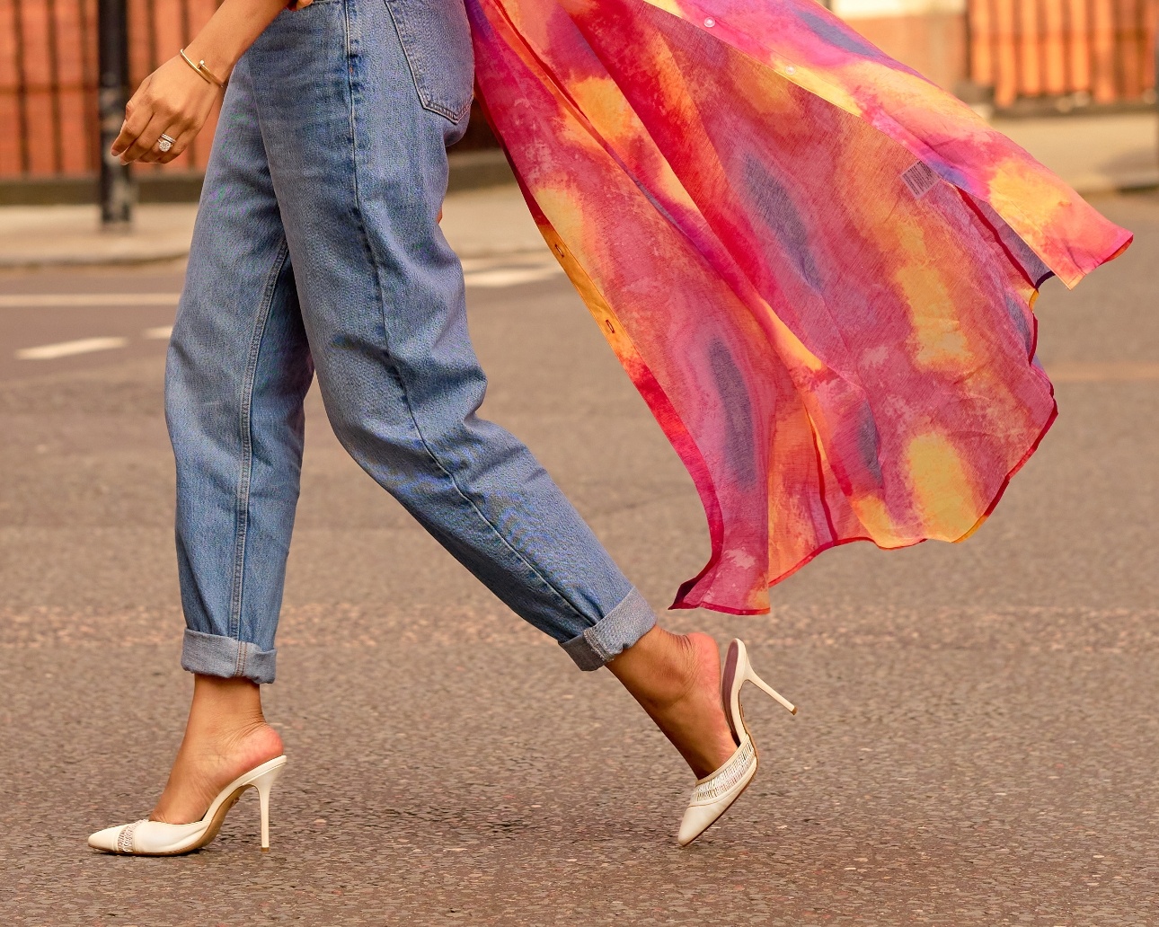 model wearing jeans and pair of heeled shoes walking on a pavement