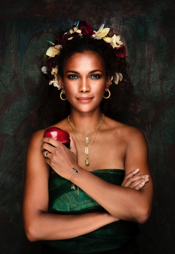 model in green dress holding red apple with floral headress and gold jewellery