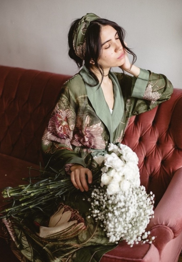 woman in silk robe on red sofa holding flowers