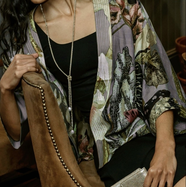 woman on chair wearing a kimono black top silver necklace and holding a bag