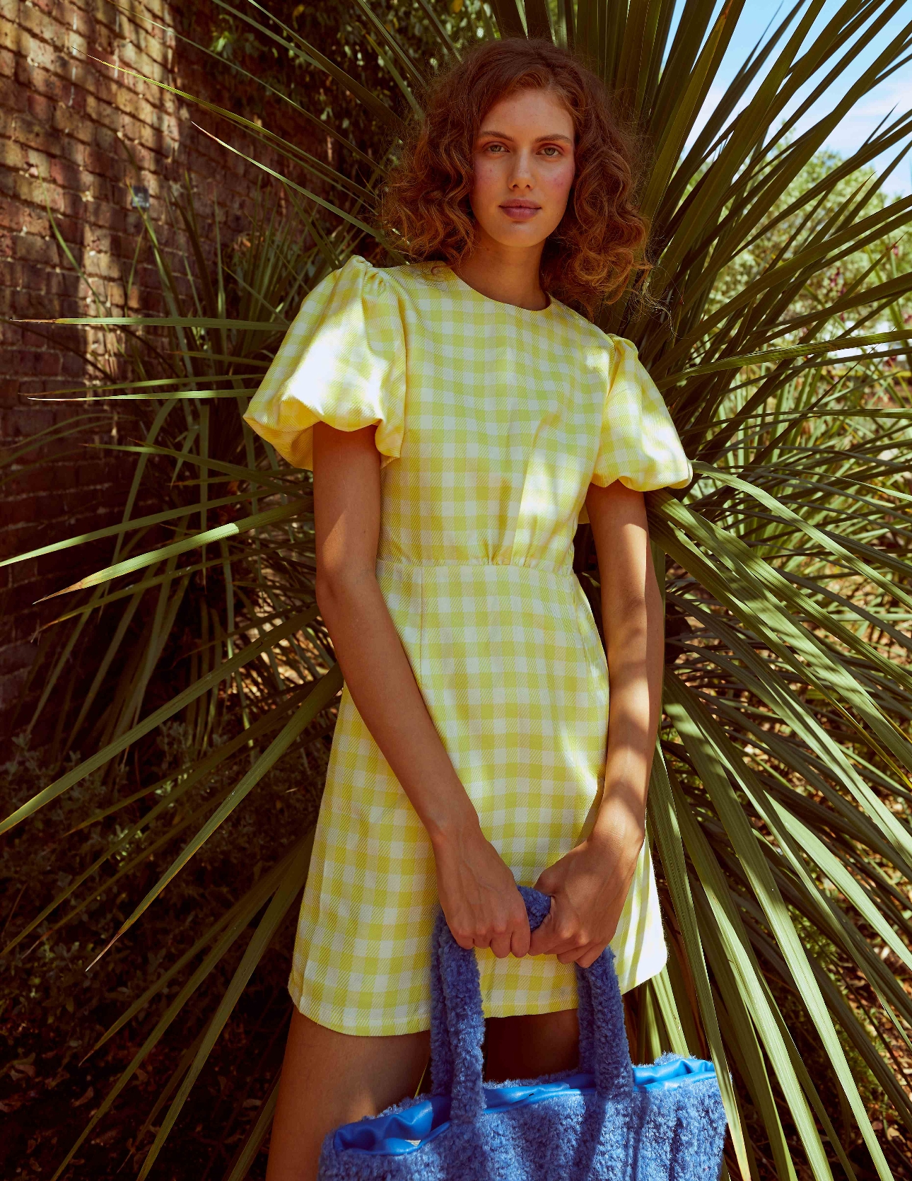 woman in yellow check dress holding blue bag