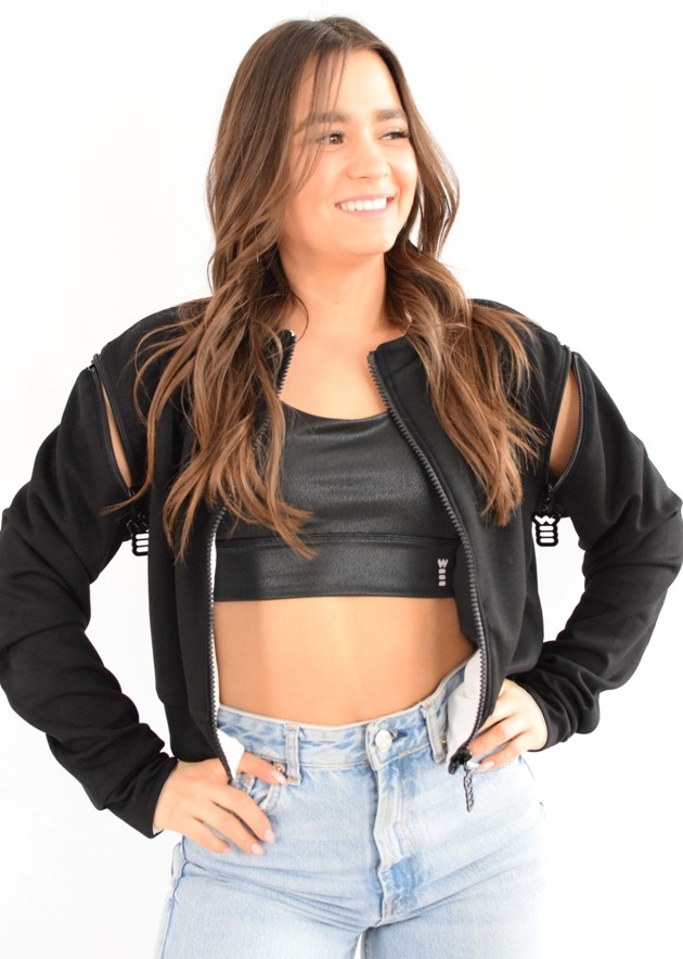 woman in sports top and jacket, and jeans, hands on hips