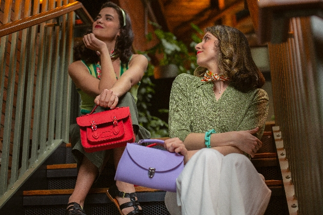 two women in 1920s clothing sat on stairs holding bags