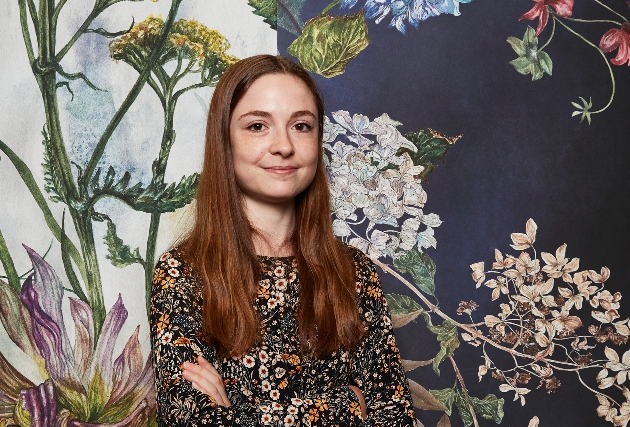 woman standing in front of floral print wallpaper