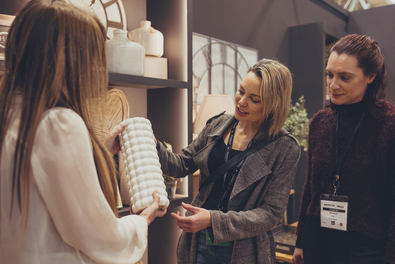 three women looking at vases at a stand at a trade show