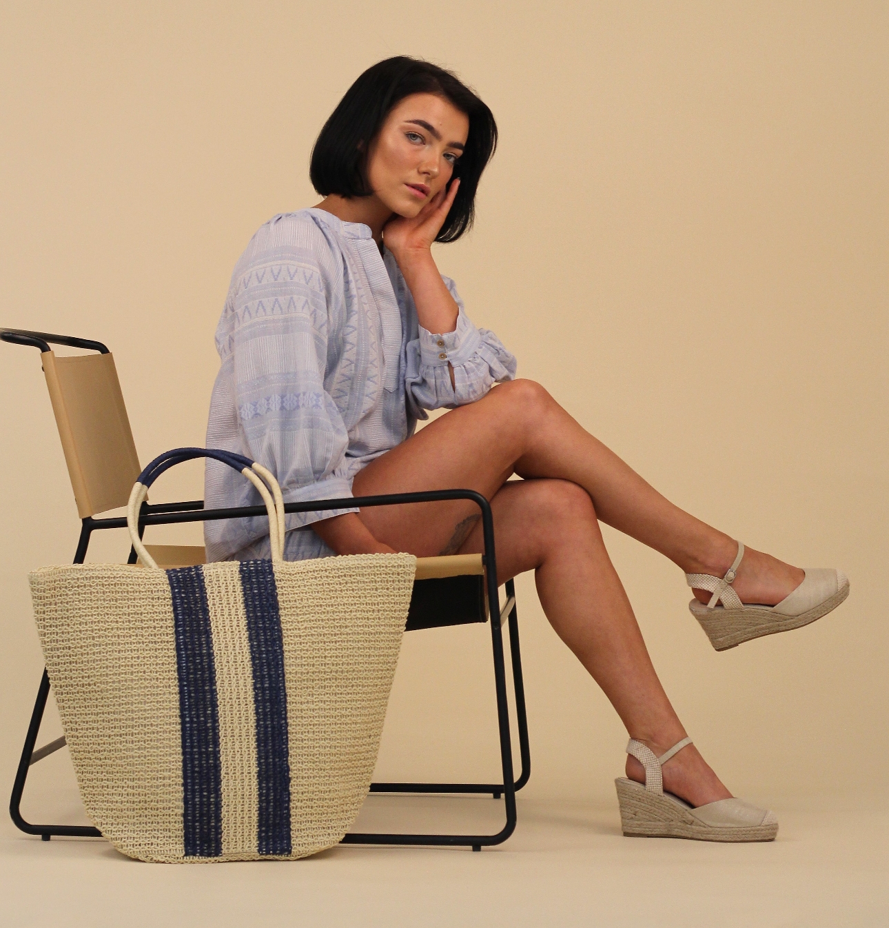 woman sat on chair wearing blue shirt denim shorts and summer sandals 