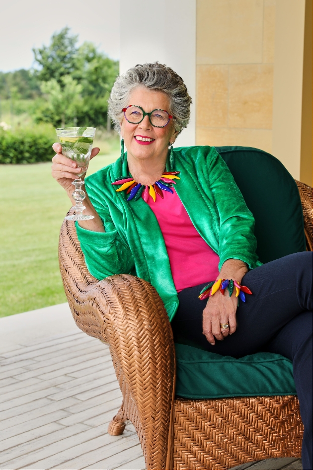 Prue Leith in a garden chair with a glass of wine wearing colourful jewellery