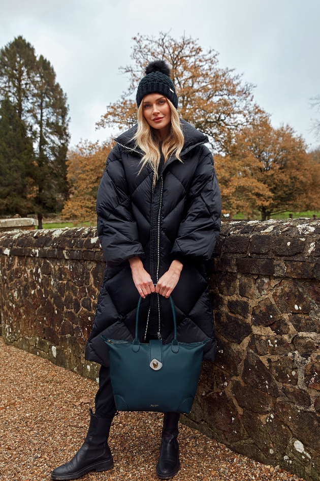 woman in winter coat and bobble hat holding green bag