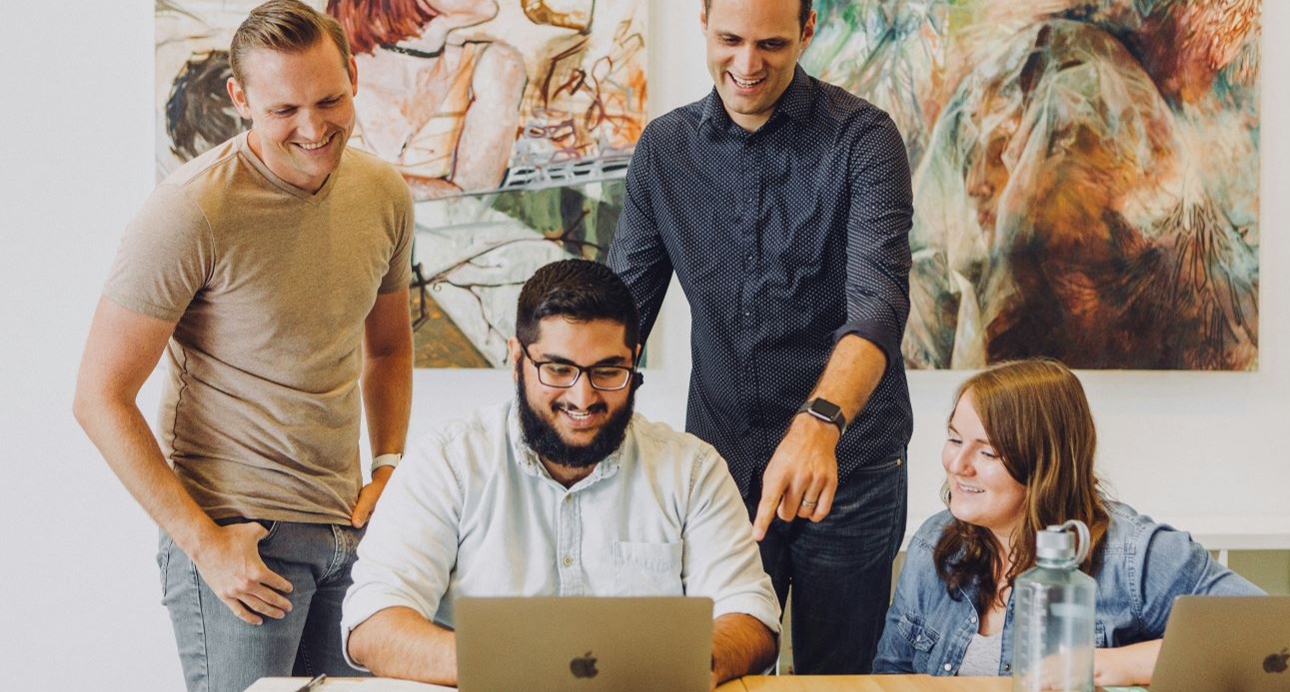 group of peopl in office all looking at one computer