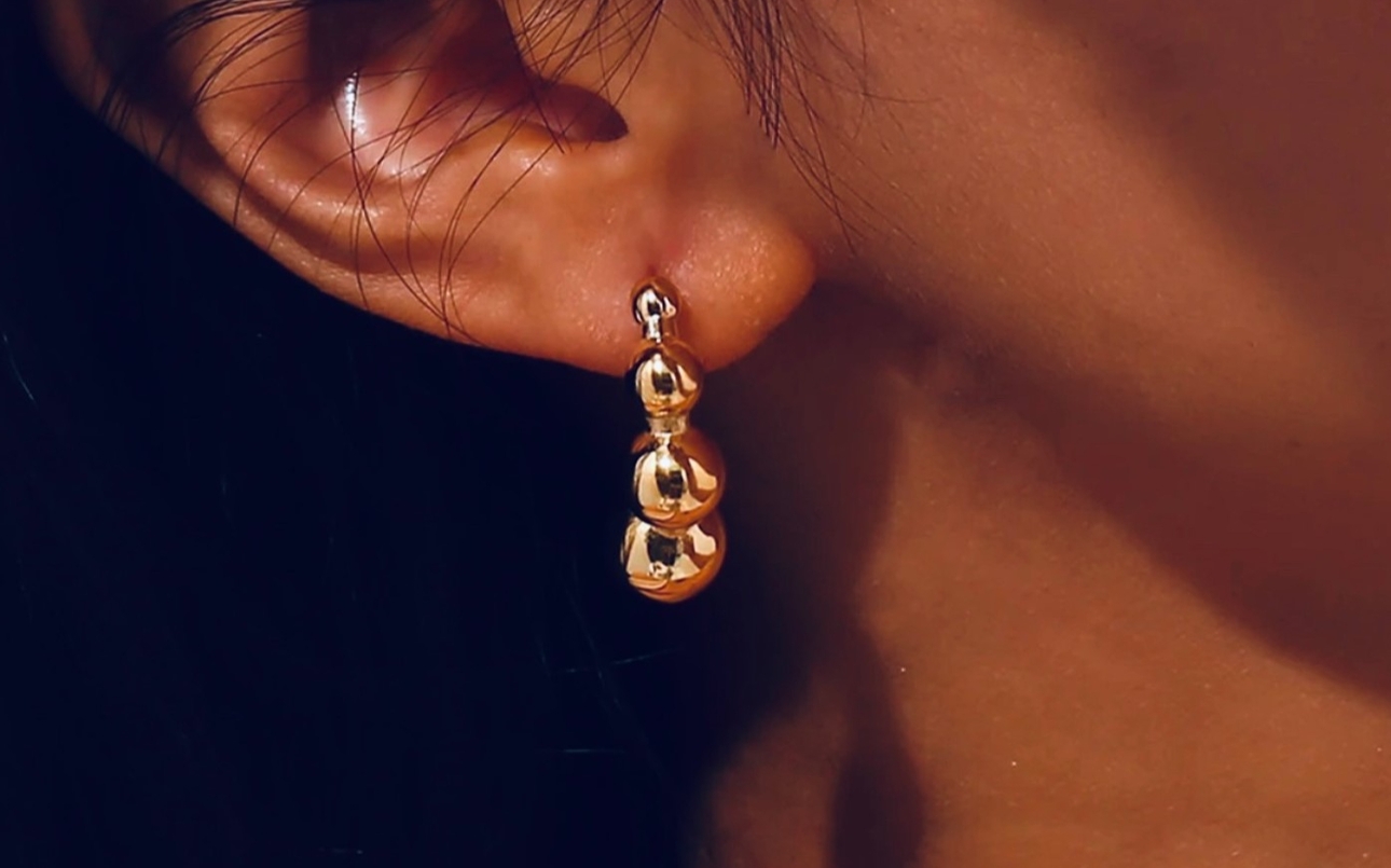 gold drop earring of three balls on an ear